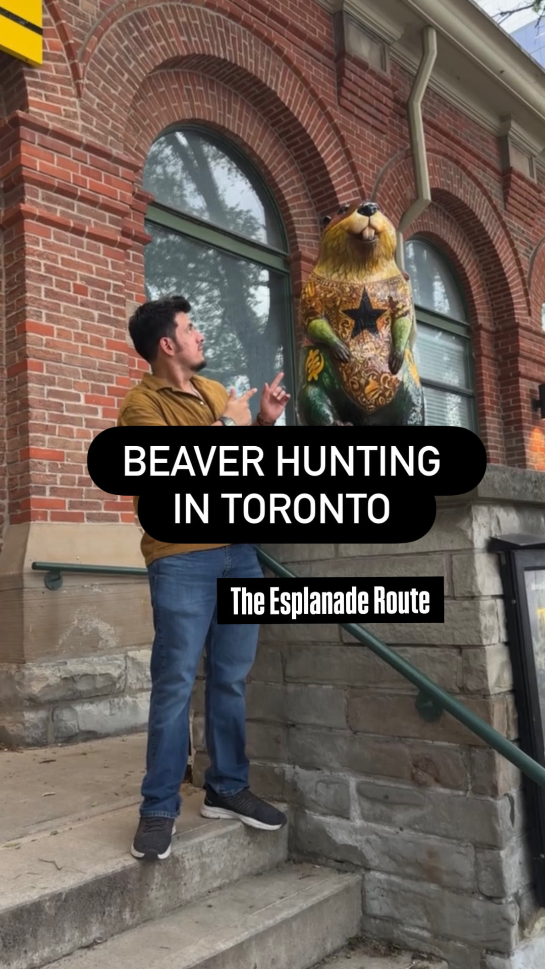 Mike pointing up at a patterned beaver sculpture on a heritage brick building along The Esplanade